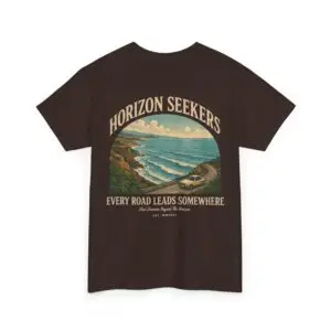 Someone wearing a blue Horizon Seekers graphic t-shirt featuring a vintage coastal road illustration with ocean cliffs, a retro car, bold typography reading "Every Road Leads Somewhere," and a nostalgic travel-inspired design in a professional studio.