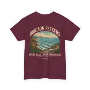 Someone wearing a blue Horizon Seekers graphic t-shirt featuring a vintage coastal road illustration with ocean cliffs, a retro car, bold typography reading "Every Road Leads Somewhere," and a nostalgic travel-inspired design in a professional studio.