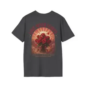 Person wearing a Love Never Leaves graphic t-shirt featuring a vintage-inspired bouquet of deep red roses, warm sunset tones, scattered rose petals, and elegant typography reading "Love Never Leaves" and "Only The Moment Does," photographed in a professional studio.