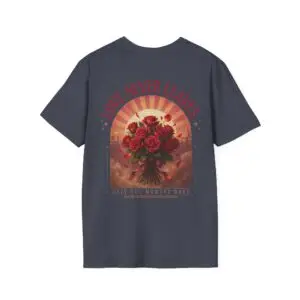 Person wearing a Love Never Leaves graphic t-shirt featuring a vintage-inspired bouquet of deep red roses, warm sunset tones, scattered rose petals, and elegant typography reading "Love Never Leaves" and "Only The Moment Does," photographed in a professional studio.