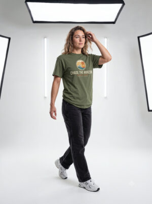 Front Image Woman wearing an olive green Chase The Horizon vintage surf graphic unisex heavy cotton t-shirt featuring a retro sunset chest print in a professional studio. Back Image Back view of woman wearing an olive green Chase The Horizon vintage surf graphic t-shirt with a large retro ocean wave and sunset illustration in a studio setting.