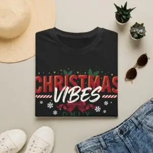 Smiling woman wearing a black Christmas Vibes Only graphic unisex t-shirt featuring festive typography, holly leaves, and snowflake accents with a Santa hat in a white studio setting.
