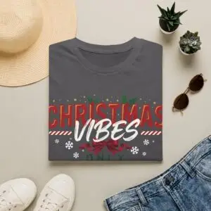 Smiling woman wearing a black Christmas Vibes Only graphic unisex t-shirt featuring festive typography, holly leaves, and snowflake accents with a Santa hat in a white studio setting.