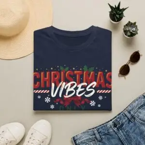 Smiling woman wearing a black Christmas Vibes Only graphic unisex t-shirt featuring festive typography, holly leaves, and snowflake accents with a Santa hat in a white studio setting.