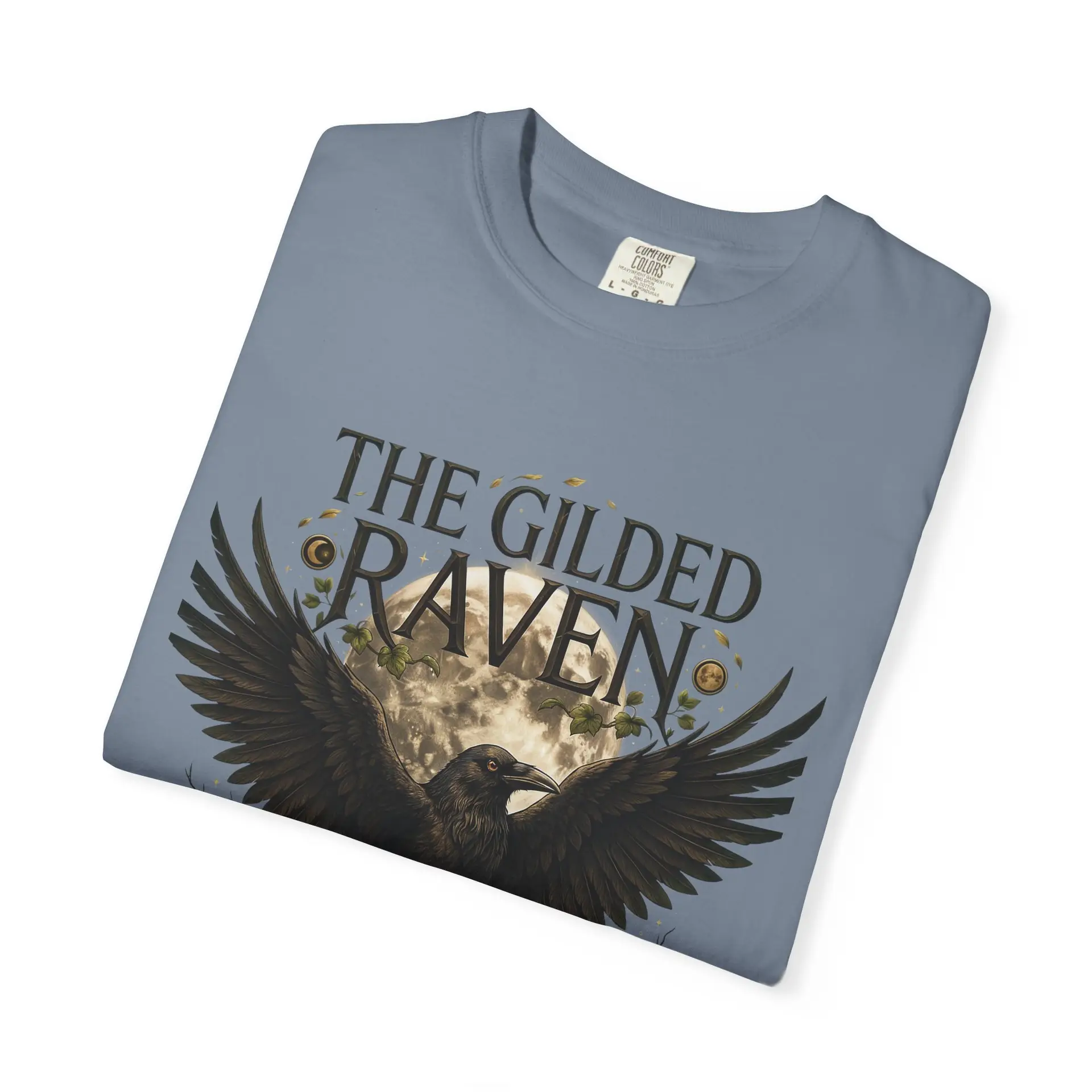 Person wearing a The Gilded Raven graphic t-shirt featuring a minimalist raven positioned before a glowing full moon with bold vintage-inspired typography reading "The Gilded Raven," photographed in a professional studio.