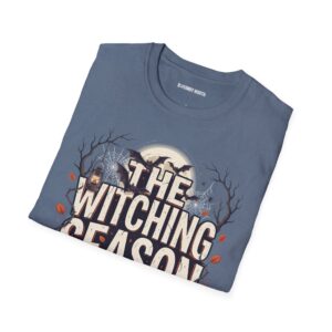 Woman wearing a blue The Witching Season Halloween graphic t-shirt featuring vintage spooky typography, a smiling jack-o'-lantern, moon, and autumn tree silhouettes in a professional studio.