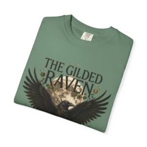 Person wearing a The Gilded Raven graphic t-shirt featuring a minimalist raven positioned before a glowing full moon with bold vintage-inspired typography reading "The Gilded Raven," photographed in a professional studio.