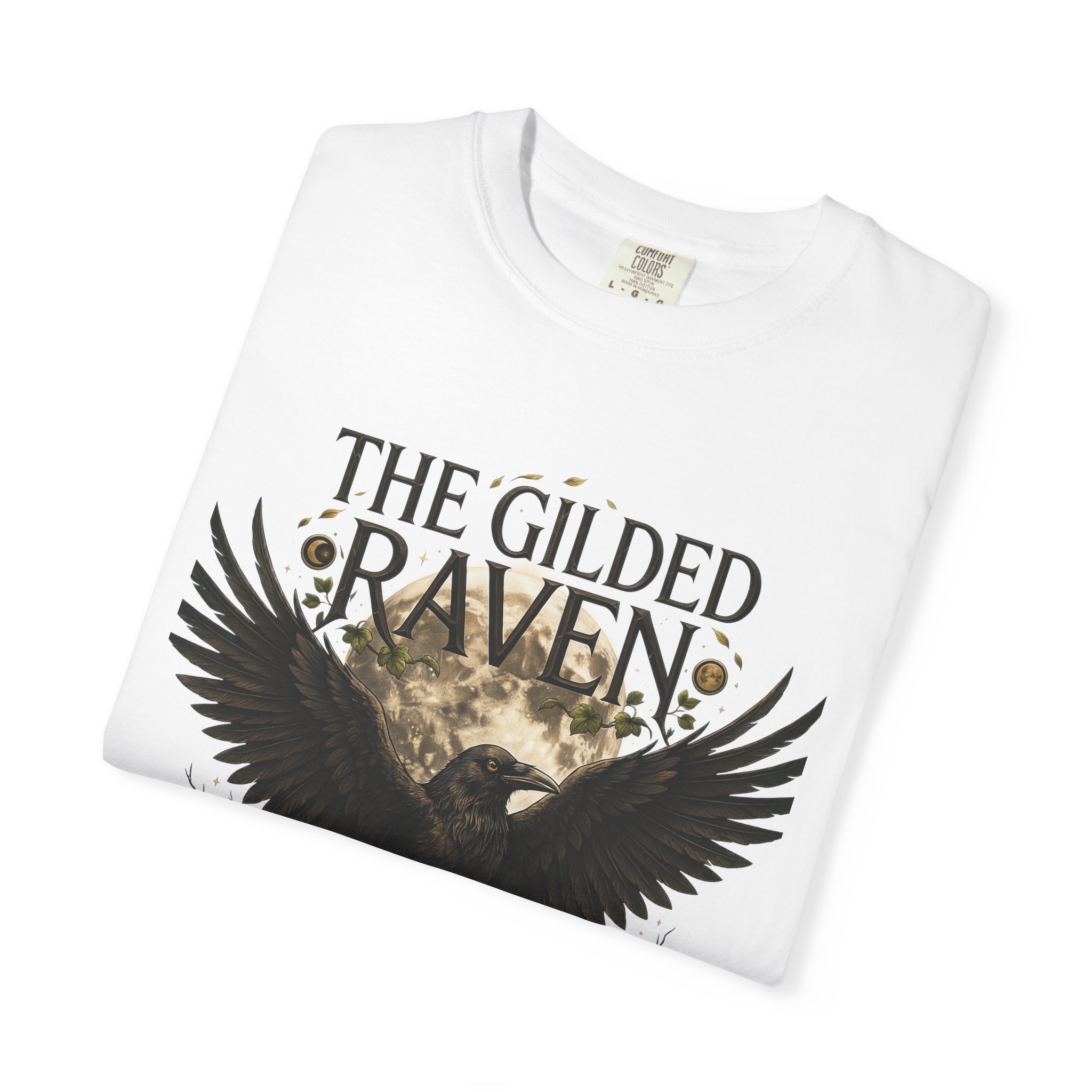 Person wearing a The Gilded Raven graphic t-shirt featuring a minimalist raven positioned before a glowing full moon with bold vintage-inspired typography reading "The Gilded Raven," photographed in a professional studio.