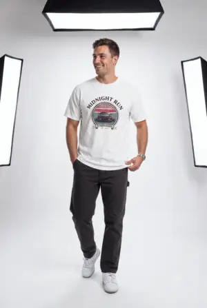 Person wearing a Midnight Run graphic t-shirt featuring a retro-inspired neon cityscape, classic late-night driving artwork, vibrant 90s color palette, and bold vintage typography, photographed in a professional studio.