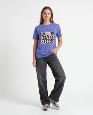 Woman wearing a purple October Never Sleeps Halloween graphic t-shirt featuring a vintage spooky typography design with moon, bats, and autumn tree silhouettes in a professional studio.