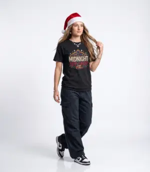 Woman wearing a black Midnight Toy Shop vintage Christmas graphic unisex t-shirt featuring retro holiday typography and festive toy store artwork while wearing a Santa hat in a white studio setting.