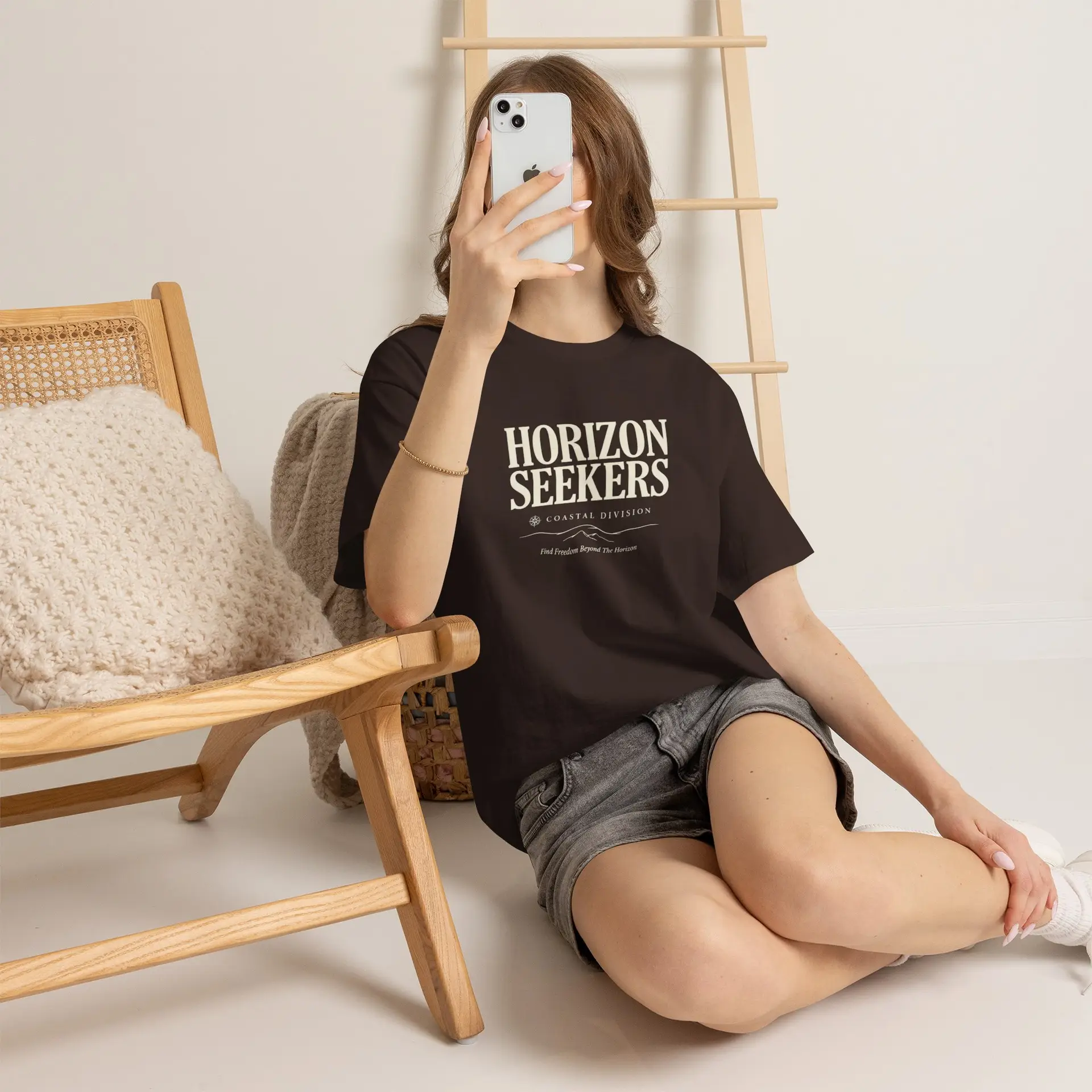 Someone wearing a blue Horizon Seekers graphic t-shirt featuring a vintage coastal road illustration with ocean cliffs, a retro car, bold typography reading "Every Road Leads Somewhere," and a nostalgic travel-inspired design in a professional studio.