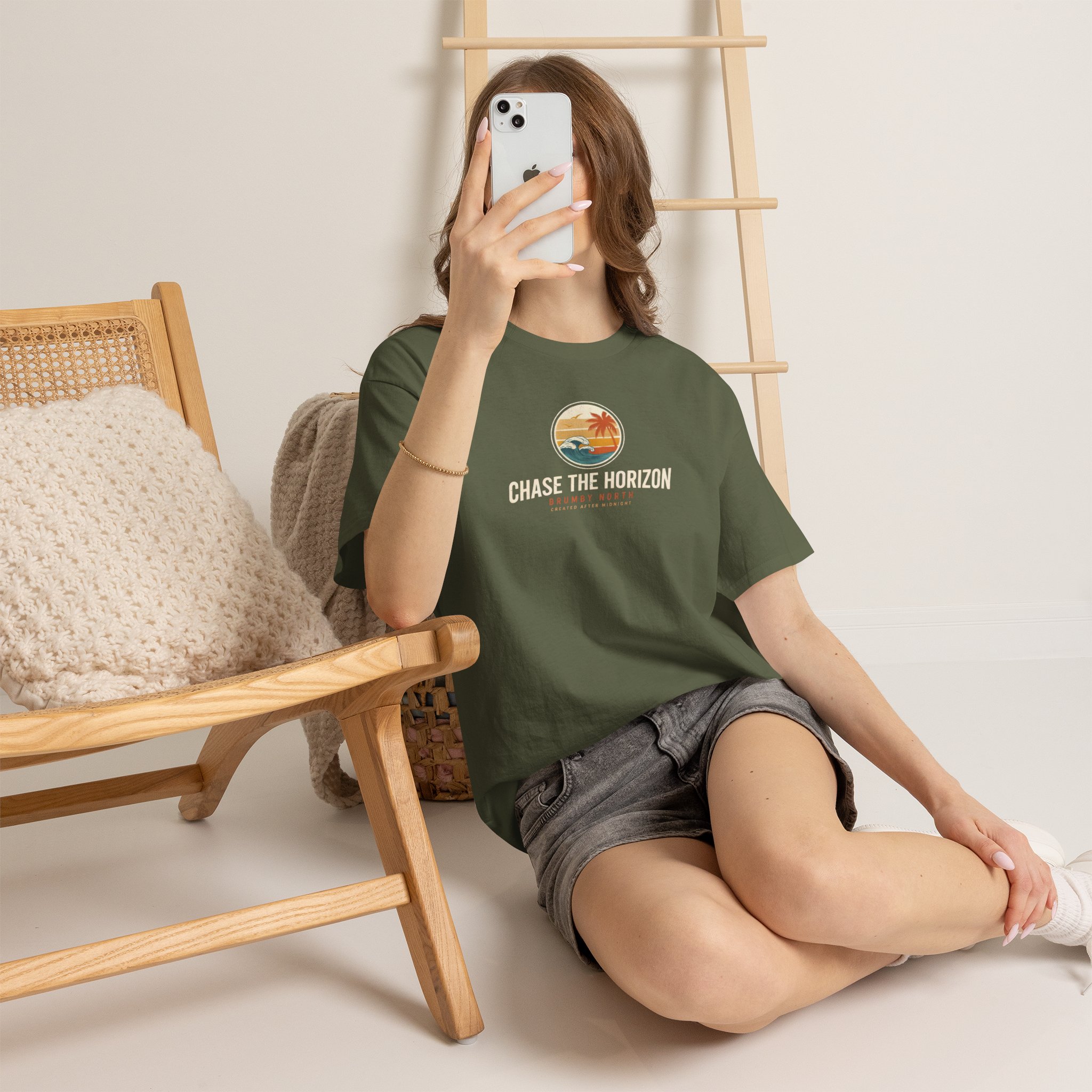 Front Image Woman wearing an olive green Chase The Horizon vintage surf graphic unisex heavy cotton t-shirt featuring a retro sunset chest print in a professional studio. Back Image Back view of woman wearing an olive green Chase The Horizon vintage surf graphic t-shirt with a large retro ocean wave and sunset illustration in a studio setting