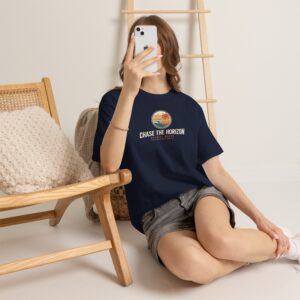 Front Image Woman wearing an olive green Chase The Horizon vintage surf graphic unisex heavy cotton t-shirt featuring a retro sunset chest print in a professional studio. Back Image Back view of woman wearing an olive green Chase The Horizon vintage surf graphic t-shirt with a large retro ocean wave and sunset illustration in a studio setting