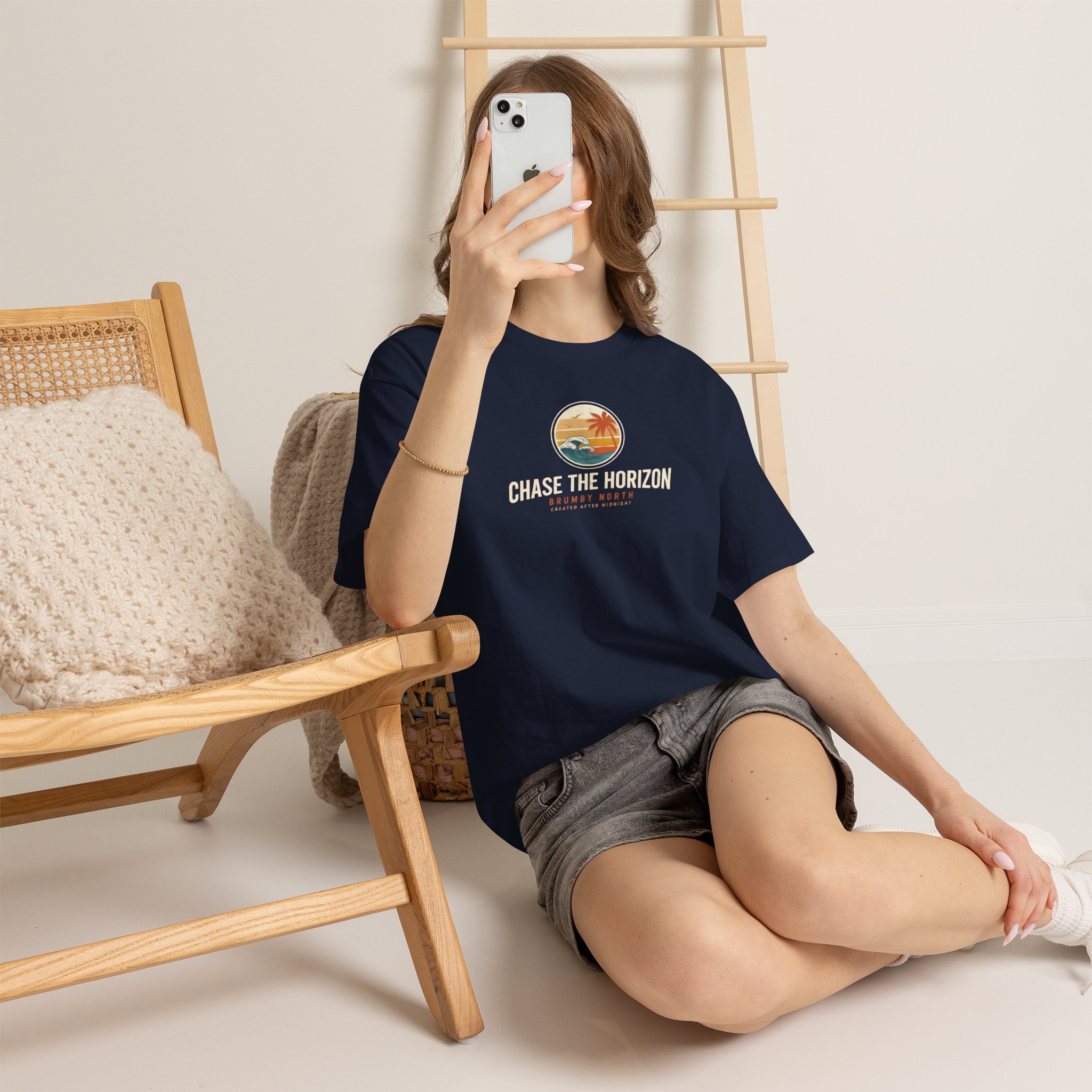 Front Image Woman wearing an olive green Chase The Horizon vintage surf graphic unisex heavy cotton t-shirt featuring a retro sunset chest print in a professional studio. Back Image Back view of woman wearing an olive green Chase The Horizon vintage surf graphic t-shirt with a large retro ocean wave and sunset illustration in a studio setting