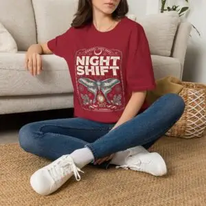 Woman wearing a red Night Shift vintage moth graphic unisex t-shirt with gothic typography and pocket watch illustration on a white studio background.