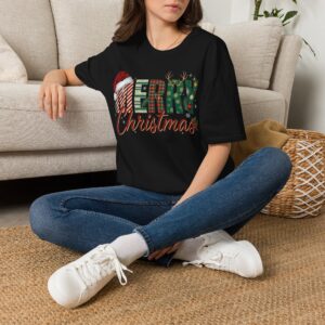 Smiling woman wearing a black Merry Christmas plaid graphic unisex t-shirt featuring festive lettering, Santa hat, reindeer antlers, and holiday decorations in a white studio setting.