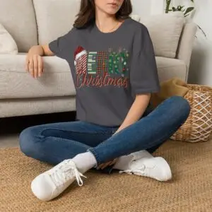 Smiling woman wearing a black Merry Christmas plaid graphic unisex t-shirt featuring festive lettering, Santa hat, reindeer antlers, and holiday decorations in a white studio setting.