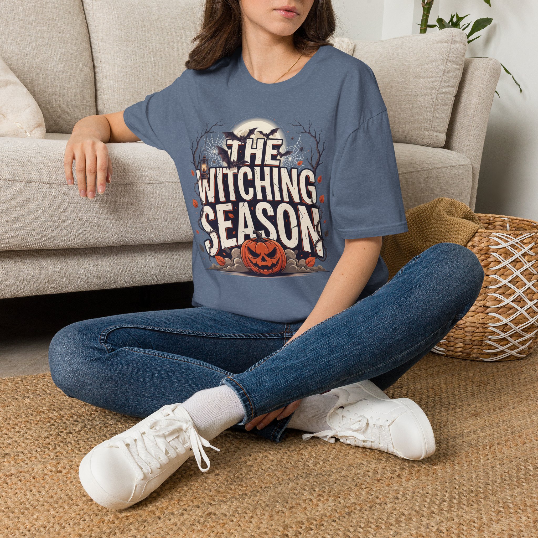 Woman wearing a blue The Witching Season Halloween graphic t-shirt featuring vintage spooky typography, a smiling jack-o'-lantern, moon, and autumn tree silhouettes in a professional studio.