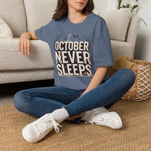Woman wearing a purple October Never Sleeps Halloween graphic t-shirt featuring a vintage spooky typography design with moon, bats, and autumn tree silhouettes in a professional studio.
