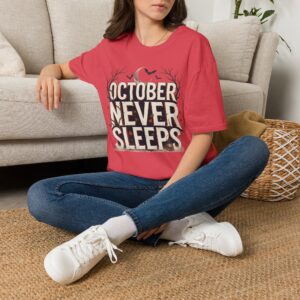 Woman wearing a purple October Never Sleeps Halloween graphic t-shirt featuring a vintage spooky typography design with moon, bats, and autumn tree silhouettes in a professional studio.