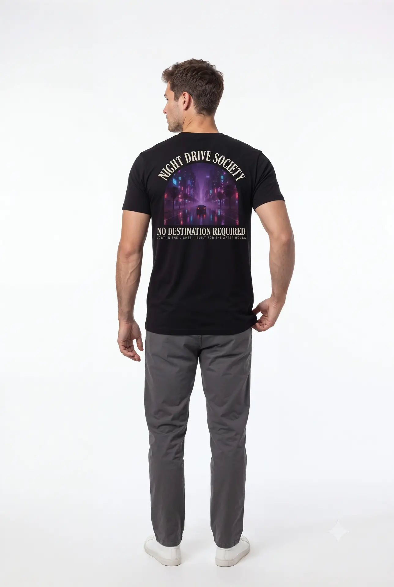 Person wearing a Night Drive Society graphic t-shirt featuring a retro-futuristic neon city skyline, rain-soaked streets, towering palm trees, and a classic car driving into the night with bold typography reading "No Destination Required" and "Lost In The Lights • Built For The After Hours," photographed in a professional studio.