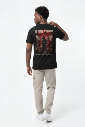 Person wearing a black No Peace In Paradise graphic t-shirt featuring a hooded figure with angel wings beneath a traditional Japanese torii gate, set against a crimson moon with ravens, floral elements, and gothic typography reading "Built From Chaos" and "Everything Beautiful Comes From Damage," photographed in a professional studio.