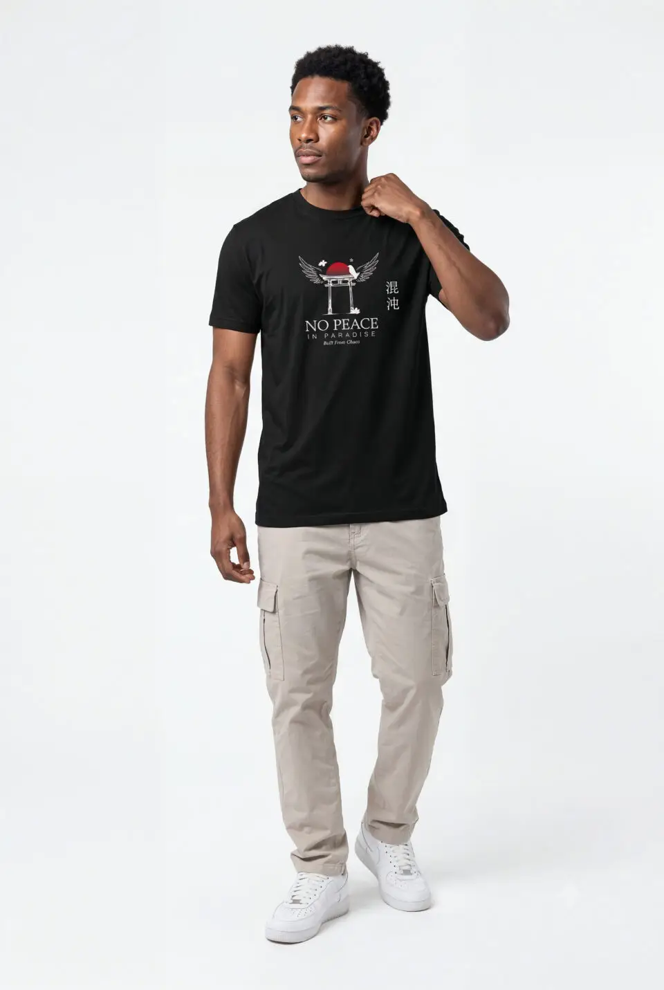 Person wearing a black No Peace In Paradise graphic t-shirt featuring a hooded figure with angel wings beneath a traditional Japanese torii gate, set against a crimson moon with ravens, floral elements, and gothic typography reading "Built From Chaos" and "Everything Beautiful Comes From Damage," photographed in a professional studio.