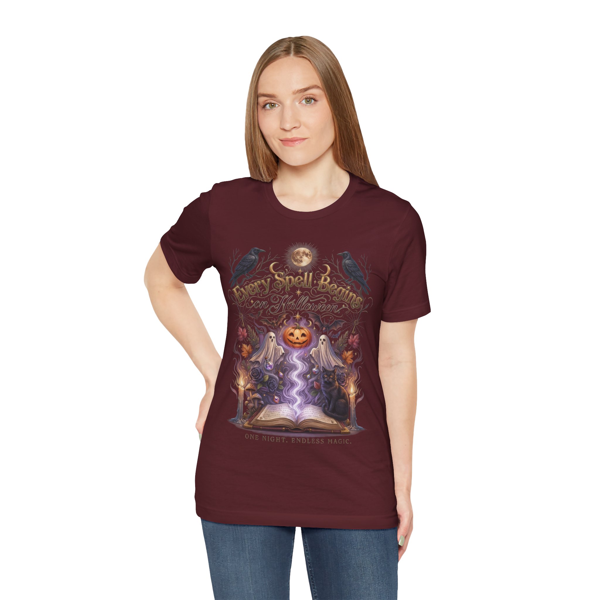 Woman wearing a black Bella+Canvas Halloween graphic t-shirt featuring a vintage illustration of an enchanted spell book, pumpkin, ghosts, candles, ravens, and the phrase "Every Spell Begins on Halloween."