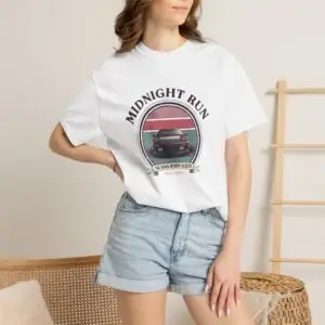 Person wearing a Midnight Run graphic t-shirt featuring a retro-inspired neon cityscape, classic late-night driving artwork, vibrant 90s color palette, and bold vintage typography, photographed in a professional studio.