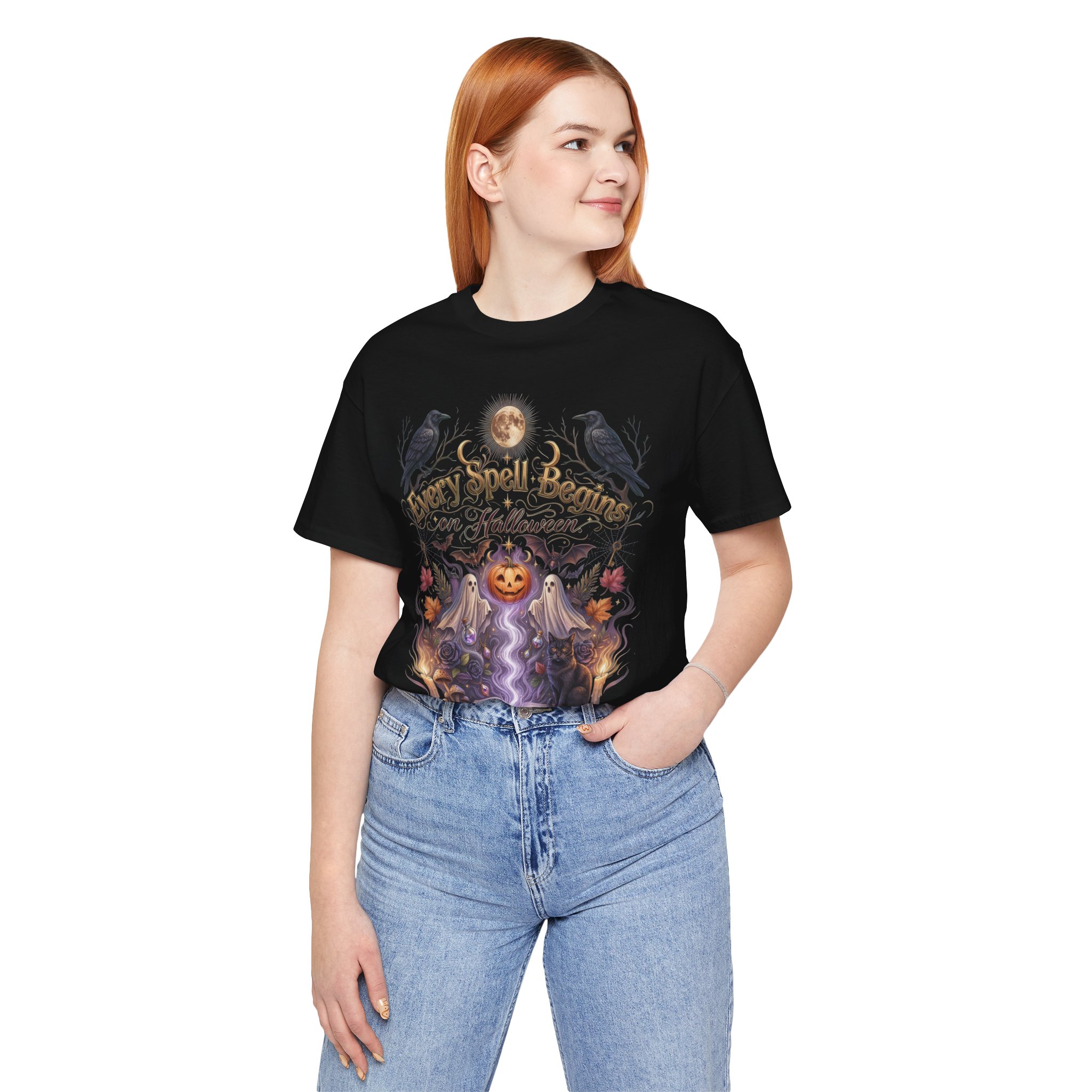 Woman wearing a black Bella+Canvas Halloween graphic t-shirt featuring a vintage illustration of an enchanted spell book, pumpkin, ghosts, candles, ravens, and the phrase "Every Spell Begins on Halloween."
