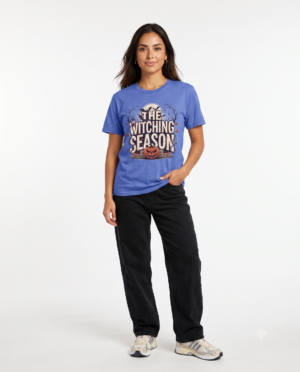 Woman wearing a blue The Witching Season Halloween graphic t-shirt featuring vintage spooky typography, a smiling jack-o'-lantern, moon, and autumn tree silhouettes in a professional studio.