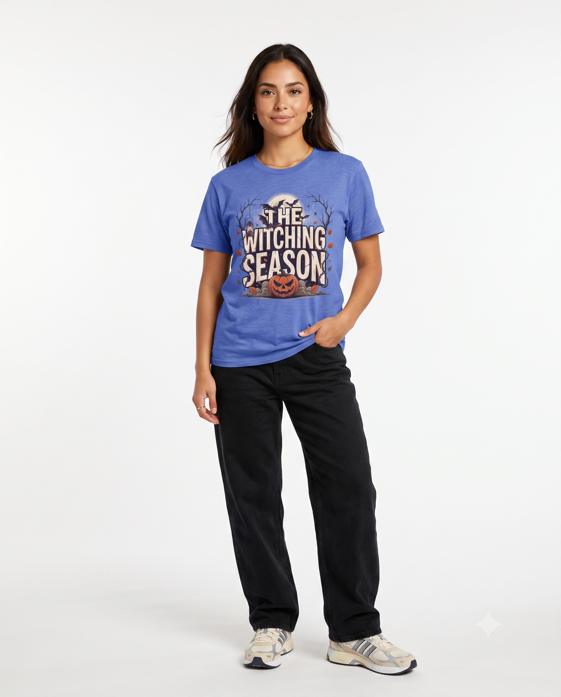 Woman wearing a blue The Witching Season Halloween graphic t-shirt featuring vintage spooky typography, a smiling jack-o'-lantern, moon, and autumn tree silhouettes in a professional studio.