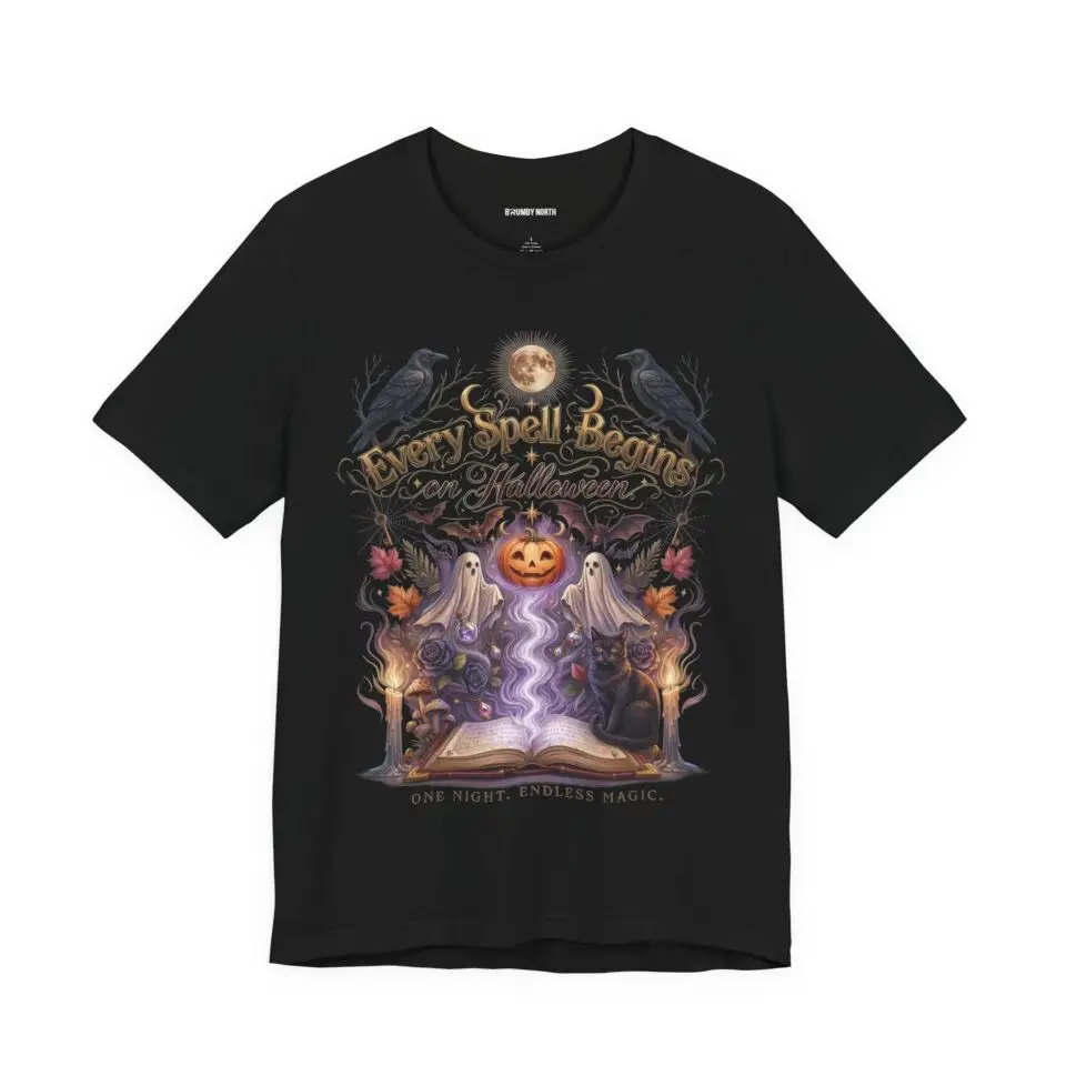 Woman wearing a black Bella+Canvas Halloween graphic t-shirt featuring a vintage illustration of an enchanted spell book, pumpkin, ghosts, candles, ravens, and the phrase "Every Spell Begins on Halloween."