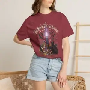 Comfort Colors 1717 black garment-dyed Halloween t-shirt featuring The Black Flame Society graphic with black cats, candles, purple flame, pumpkins, spell books, and witchy aesthetic artwork