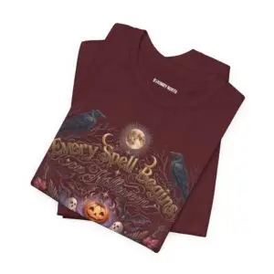 Woman wearing a black Bella+Canvas Halloween graphic t-shirt featuring a vintage illustration of an enchanted spell book, pumpkin, ghosts, candles, ravens, and the phrase "Every Spell Begins on Halloween."