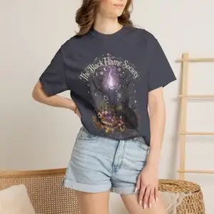 Comfort Colors 1717 black garment-dyed Halloween t-shirt featuring The Black Flame Society graphic with black cats, candles, purple flame, pumpkins, spell books, and witchy aesthetic artwork