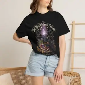 Comfort Colors 1717 black garment-dyed Halloween t-shirt featuring The Black Flame Society graphic with black cats, candles, purple flame, pumpkins, spell books, and witchy aesthetic artwork
