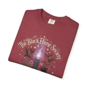 Comfort Colors 1717 black garment-dyed Halloween t-shirt featuring The Black Flame Society graphic with black cats, candles, purple flame, pumpkins, spell books, and witchy aesthetic artwork