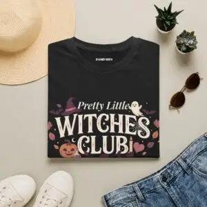 Pink Gildan Softstyle Halloween t-shirt featuring the "Pretty Little Witches Club" graphic with pumpkins, ghosts, bats, stars, and cute spooky fall artwork.