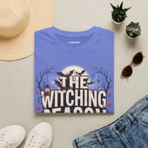 Witching Season Halloween graphic t-shirt featuring vintage spooky typography, a smiling jack-o'-lantern, moon, and autumn tree silhouettes in a professional studio.