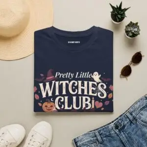 Pink Gildan Softstyle Halloween t-shirt featuring the "Pretty Little Witches Club" graphic with pumpkins, ghosts, bats, stars, and cute spooky fall artwork.