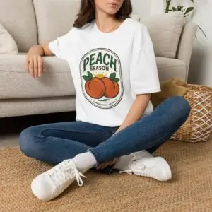Peach Season vintage graphic T-shirt worn by a female model with relaxed black jeans in a studio setting. Shorter SEO Alt Text Peach Season vintage fruit graphic unisex T-shirt