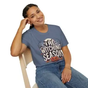 Witching Season Halloween graphic t-shirt featuring vintage spooky typography, a smiling jack-o'-lantern, moon, and autumn tree silhouettes in a professional studio.